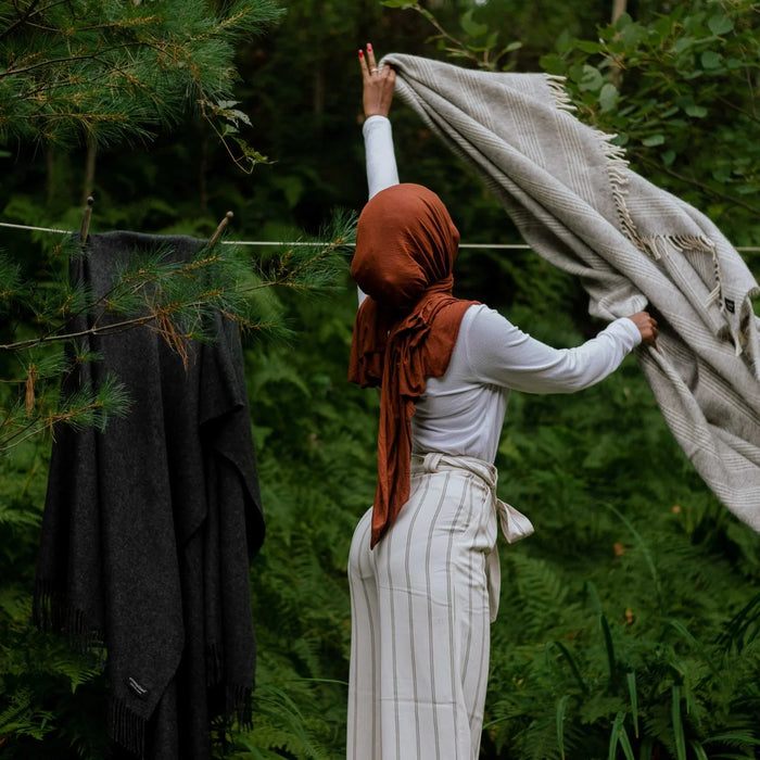 A woman is pictured hanging throws to dry with clothespins in a serene forest setting.